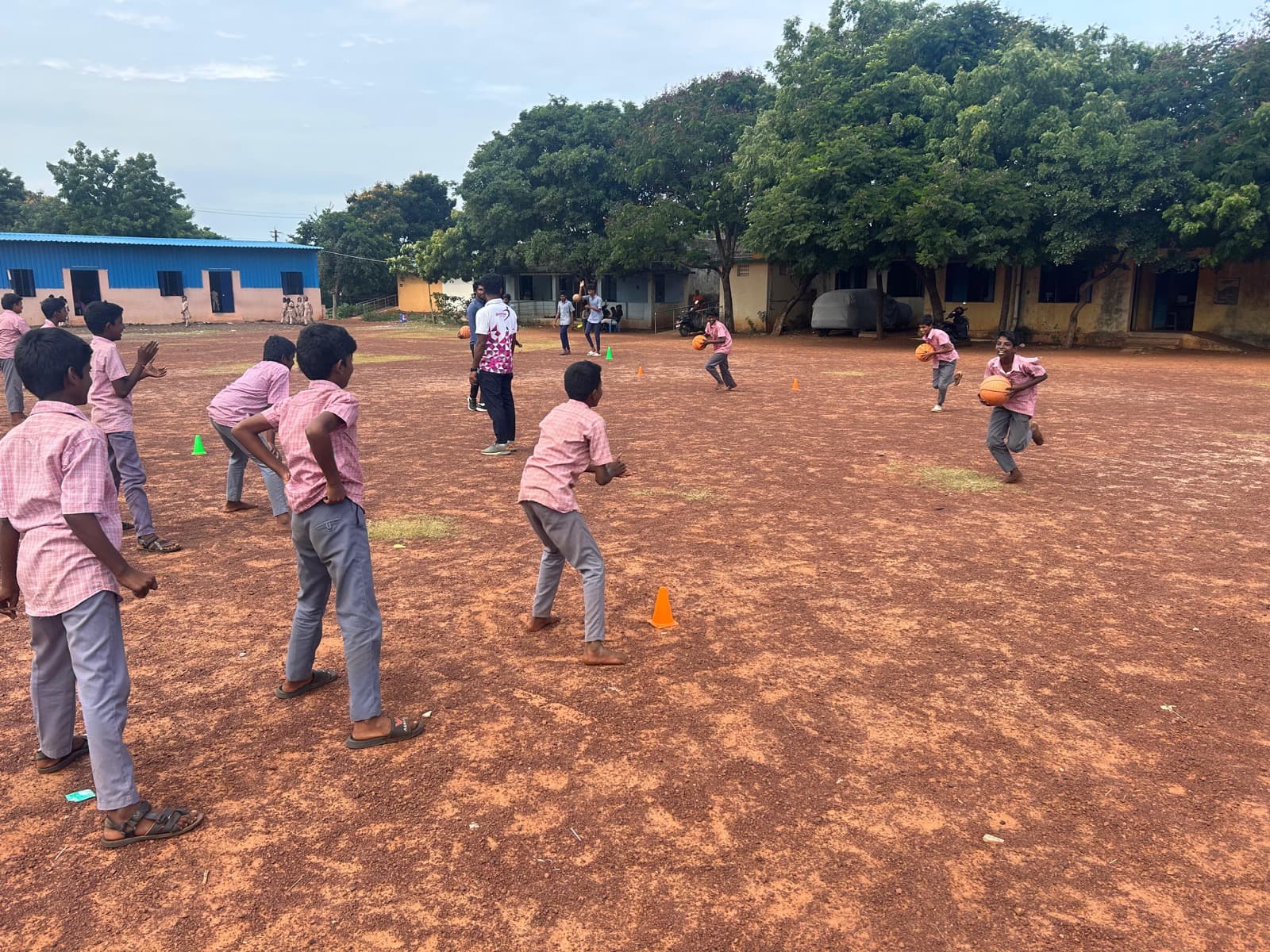 Boys playing basketball on a school ground with an SIO coach looking on